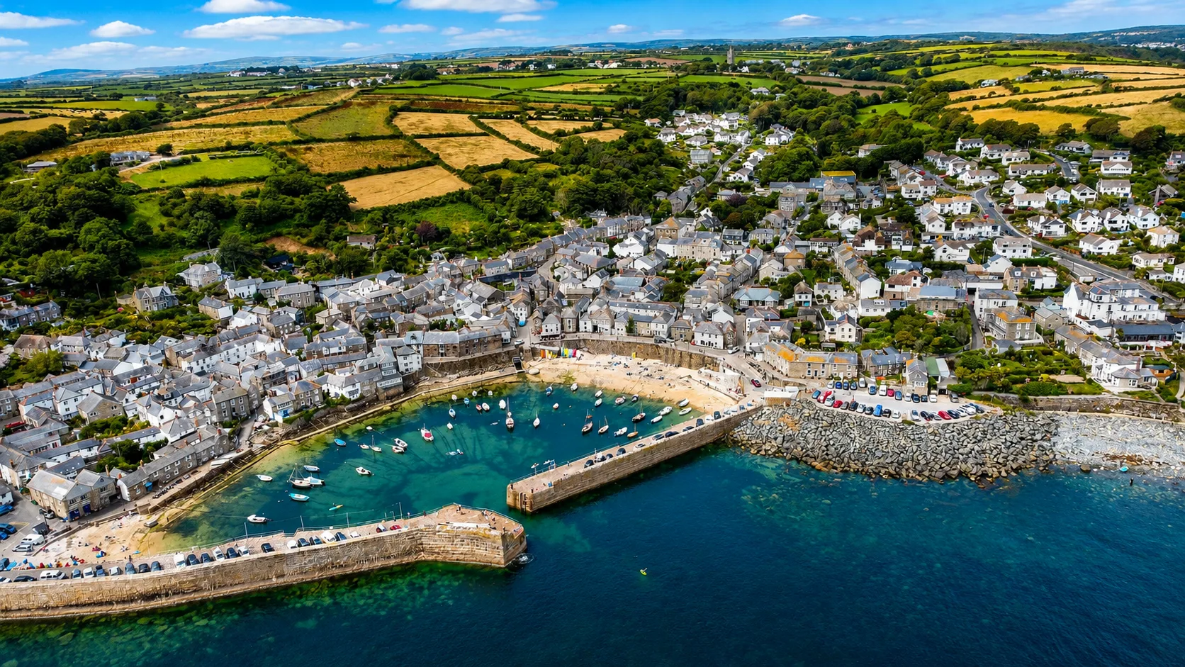 Aerial view of a Cornish harbour village with sea, fields and countryside